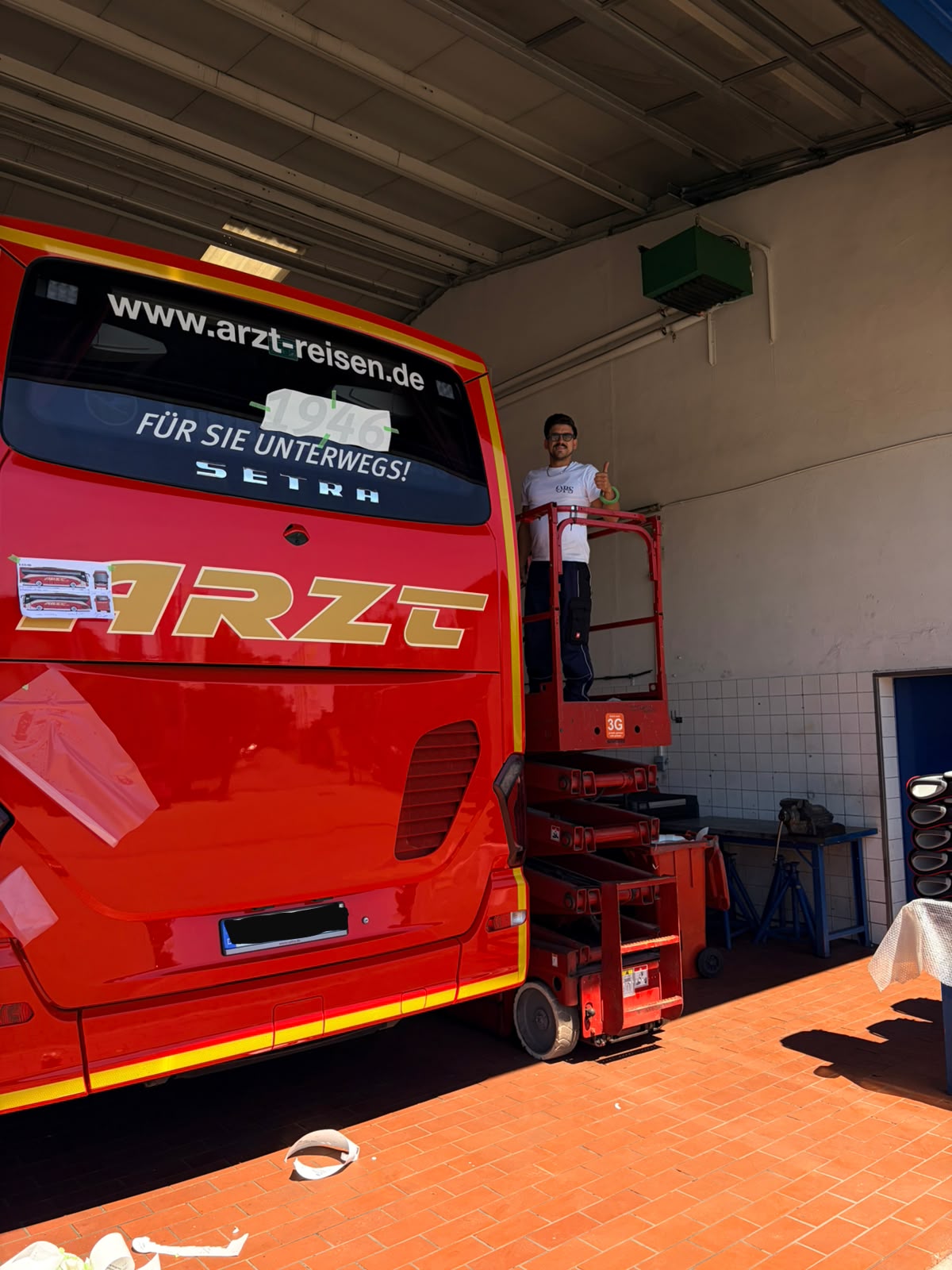 Osmar bei der Montage einer Folierung am Heck eines roten Arzt-Reisen-Reisebusses