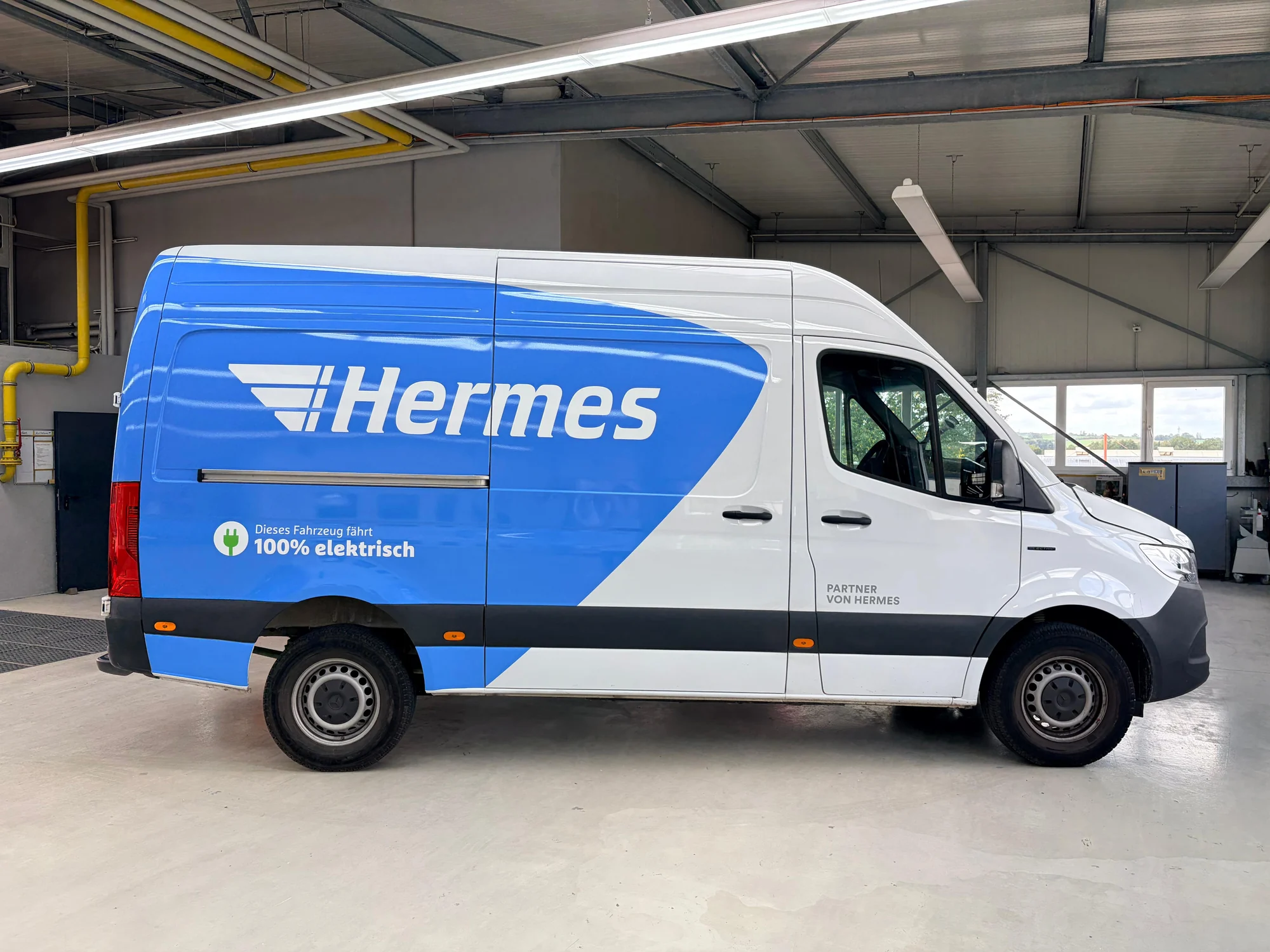 Weißer Hermes-Elektrotransporter mit blauer Markenfolierung und weißem Schriftzug in der Seitenansicht